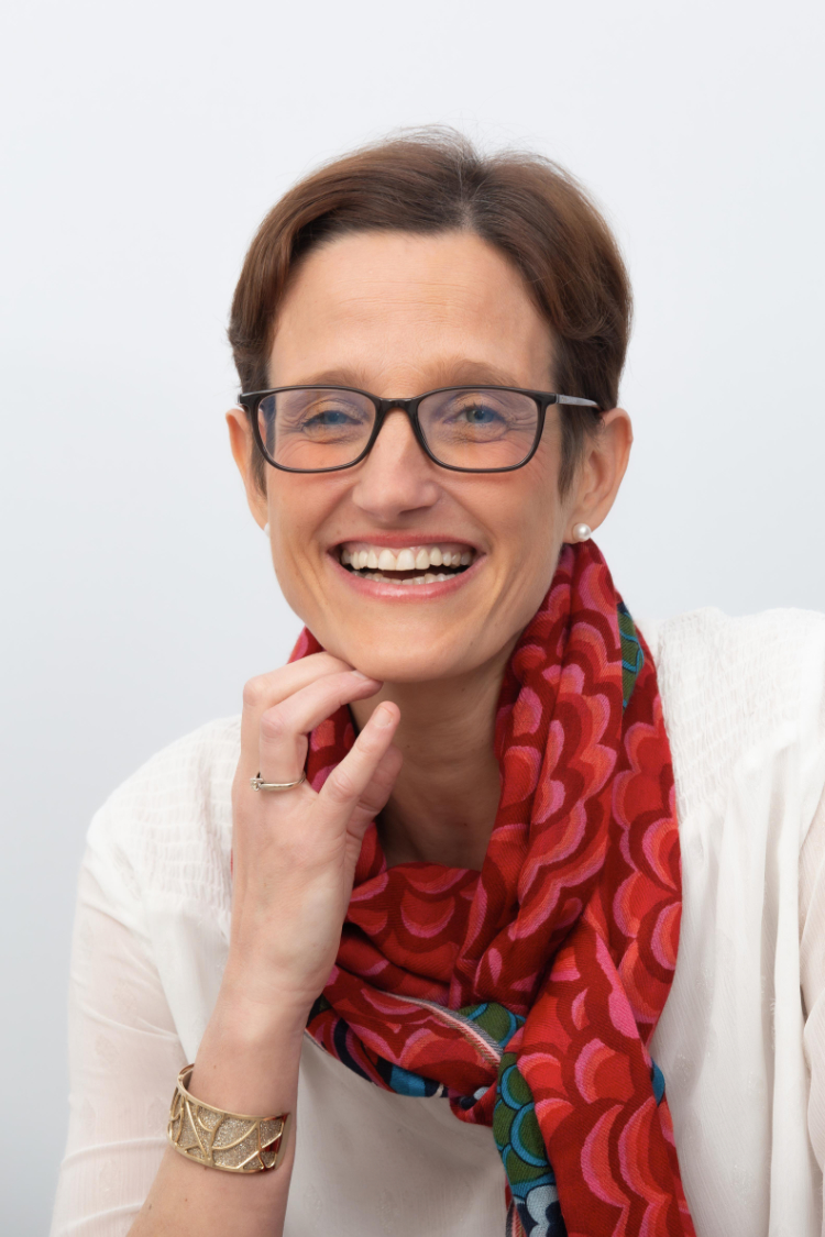 portrait d'une femme tout sourire, cheveux courts, lunettes, écharpe rouge à motif, large bracelet